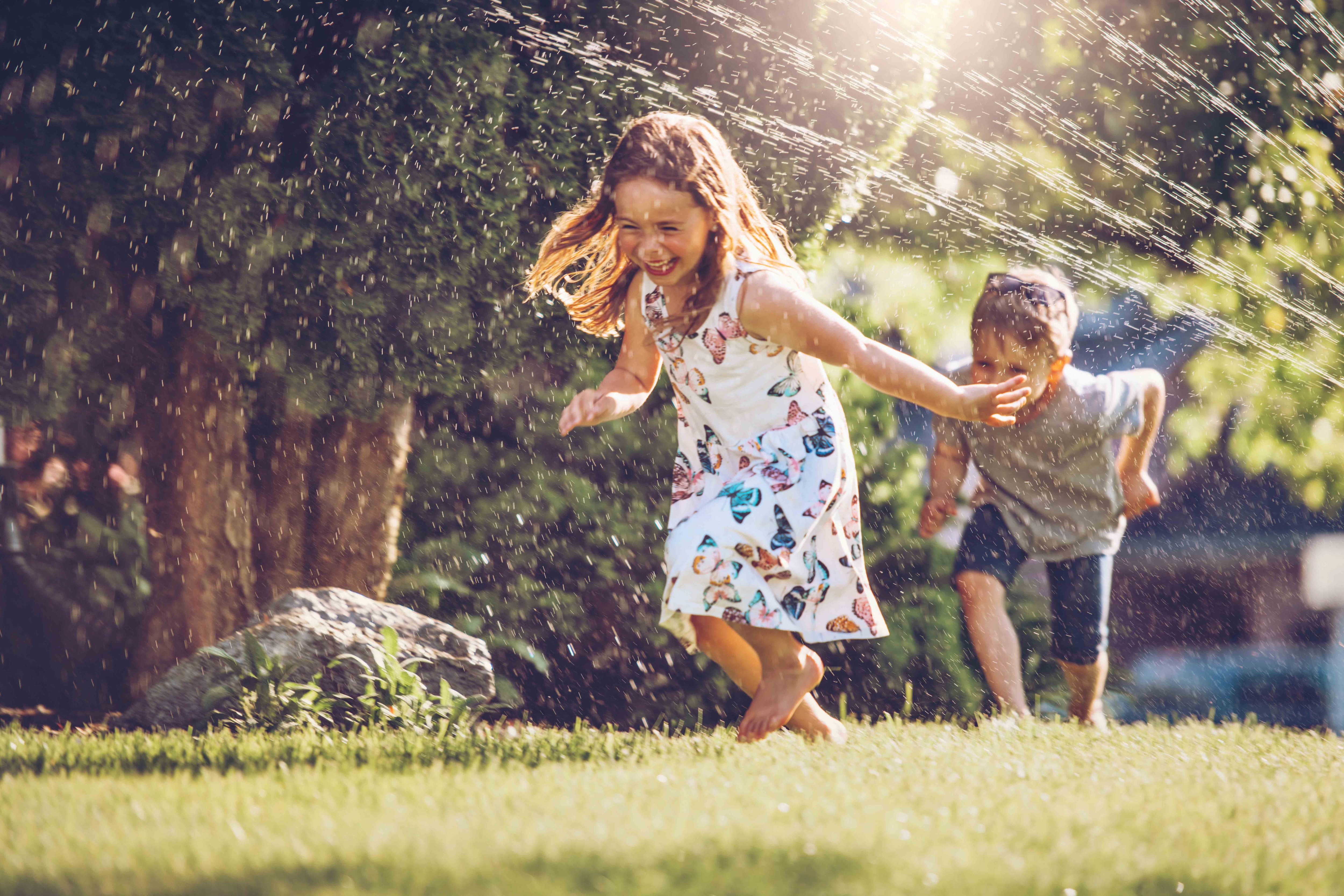 Two kids running through a sprinkler